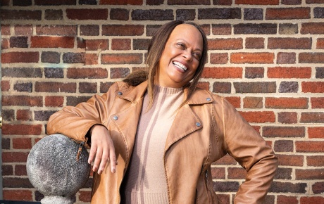 Image of Brenda Barbour smiling with her hand on her hip and a brick wall. 
