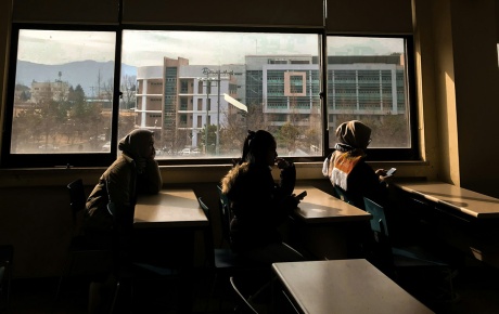 Image of three kids sitting at desks with a window behind them. Photo by Nanda Amelia.